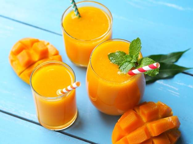 Suco de manga com manga fresca madura cortada em uma mesa de madeira de cor azul para o conceito de bebidas de verão