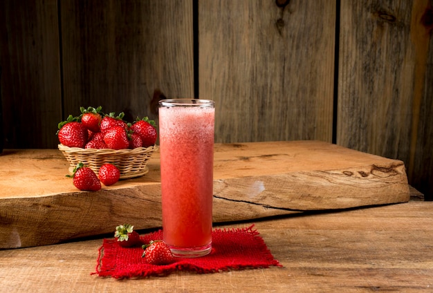 Foto suco de morango no copo na madeira com cesta de morangos ao fundo.