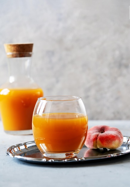 Suco de pêssego em um copo na bandeja de prata com pêssegos maduros