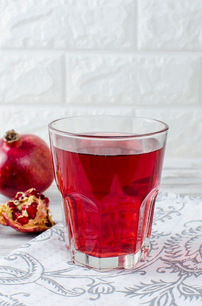 Suco de romã em vidro e romãs em fundo branco de madeira