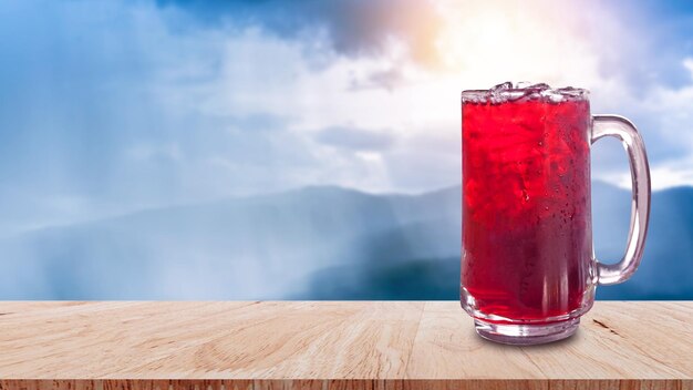 Suco de rosela fresco água doce e gelada em copo em mesa de madeira com fundo de natureza Bebidas de saúde de verão com gelo Suco vermelho com cubos de gelo em copo