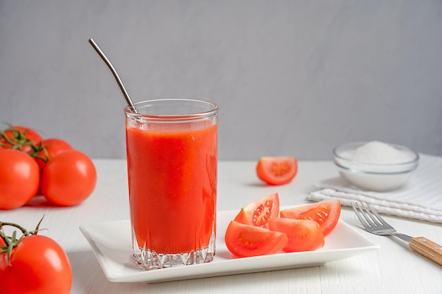 Suco de tomate caseiro refrescante em um copo com canudo de metal na mesa de madeira branca com sal