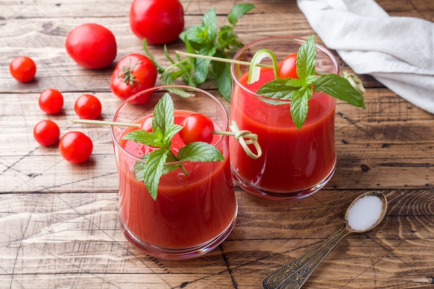 Suco de tomate com hortelã em vidro e tomates frescos em uma mesa de madeira. Conceito de alimentos orgânicos saudáveis