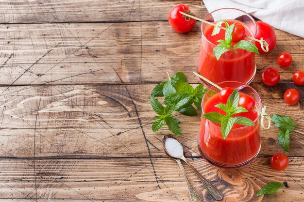 Suco de tomate com hortelã em vidro e tomates frescos em uma mesa de madeira. Conceito de alimentos orgânicos saudáveis
