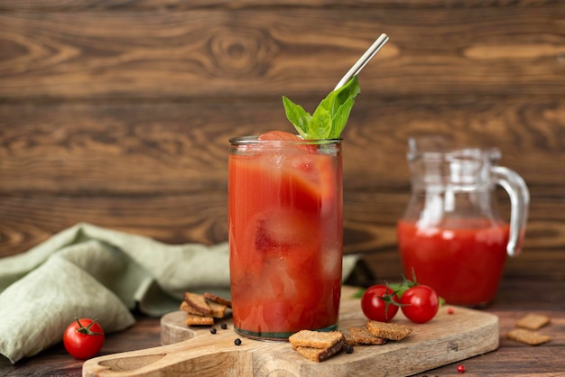 Suco de tomate com manjericão e croutons em um copo sobre uma mesa de madeira