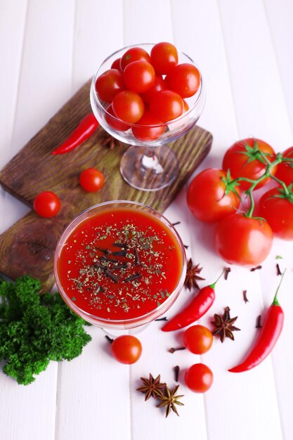 Suco de tomate em cálice e legumes frescos na tábua sobre fundo de madeira