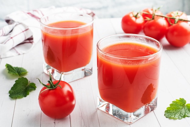 Suco de tomate em copos de vidro e tomates frescos maduros em um galho.