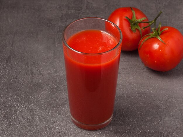 Suco de tomate em um copo decorado com tomates em um fundo cinza