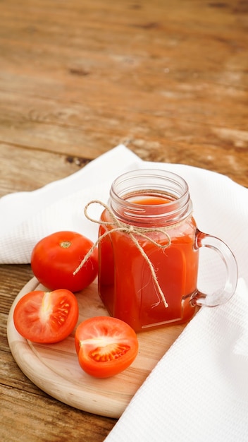 Suco de tomate em uma jarra de vidro e tomates frescos em uma tábua de madeira