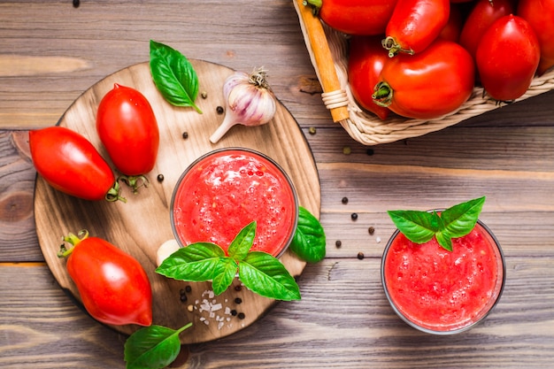 Suco de tomate fresco com folhas de manjericão em copos e ingredientes para a sua preparação em uma mesa de madeira. Vista do topo