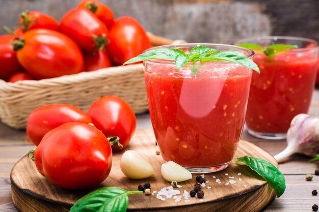 Suco de tomate fresco com folhas de manjericão em copos e ingredientes para a sua preparação em uma mesa de madeira