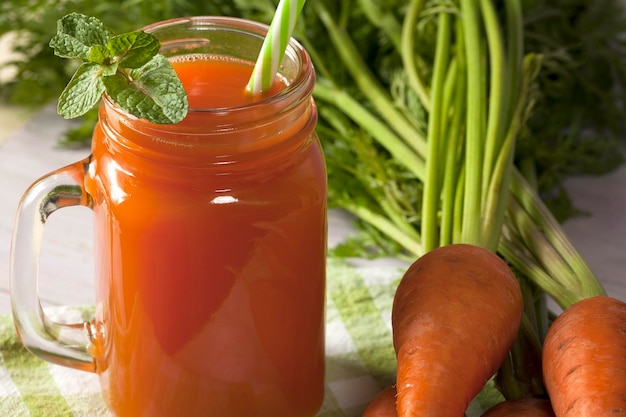 Suco delicioso e saudável de cenouras jovens Bebida de laranja Suco de cenoura Cenouras frescas com folhas verdes Comida saudável