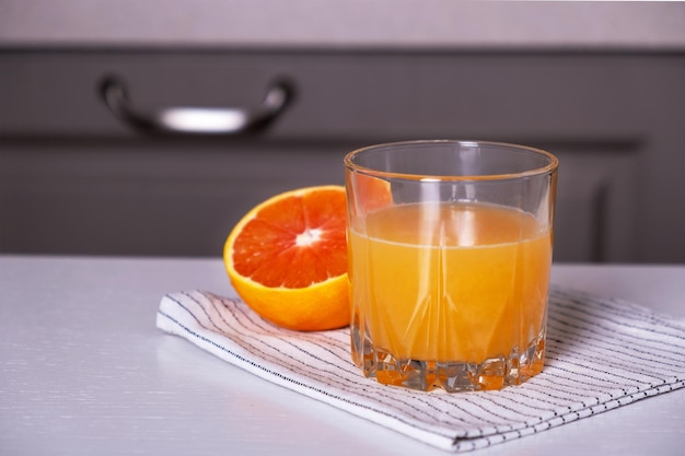 Suco espremido na hora em copo de vidro e metade de laranja em guardanapo na mesa da cozinha Foco seletivo