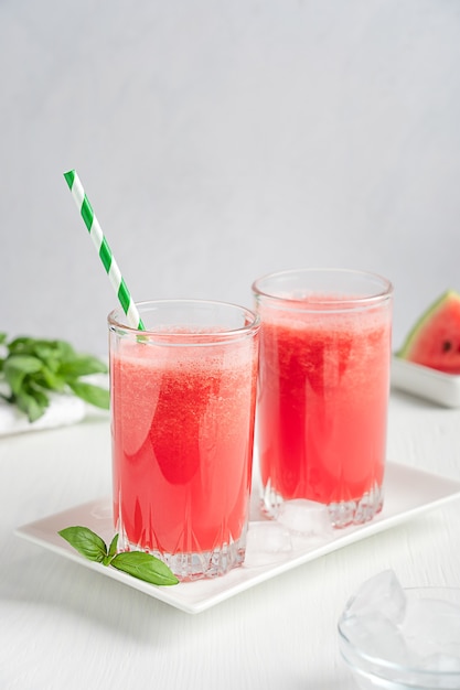 Suco refrescante de melancia servido em dois copos com canudo de papel e folhas verdes de manjericão