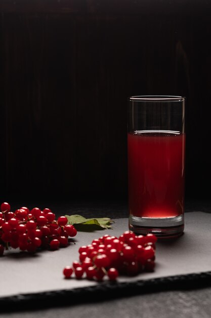 Suco vermelho de viburnum em um copo sobre uma mesa preta. Perto de bagas de viburnum. Comida saudável. Vista frontal. Copie o espaço