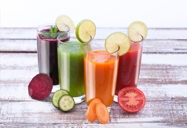 Foto sucos de vegetais e fatias de tomate, pepino, beterraba, cenoura na mesa de madeira.