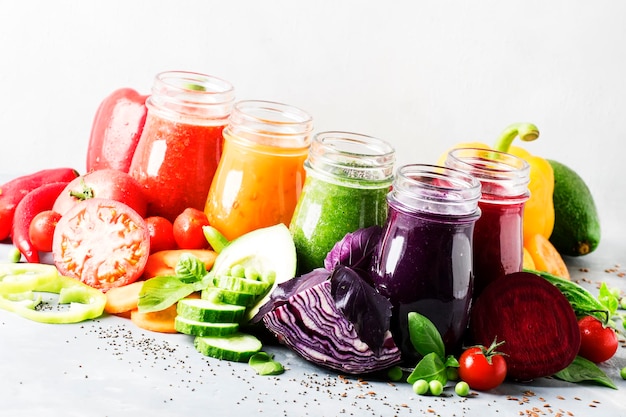 Sucos de vegetais veganos multicoloridos e smoothies em garrafas de vidro em foco seletivo de mesa cinza