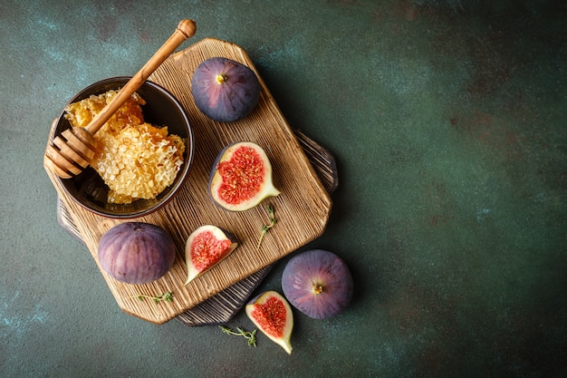 Suculentas frutas frescas de figo inteiro e figos cortados e uma tigela de mel em favos de mel na tábua de madeira. vista do topo
