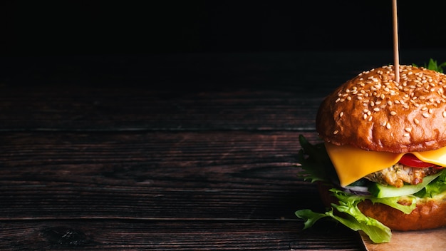 Foto suculento delicioso hambúrguer com carne, queijo, alface, tomate e cebola close-up em fundo de madeira