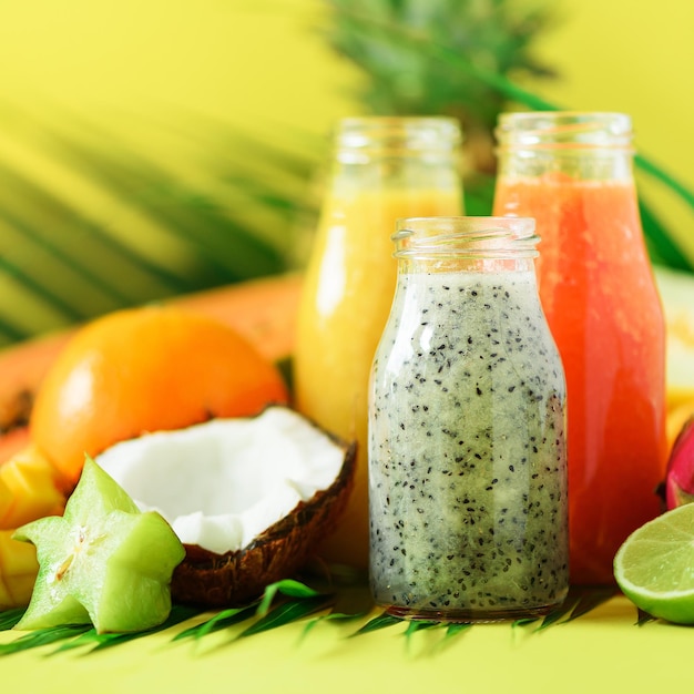 Suculento mamão e abacaxi manga laranja smoothie de frutas em frascos em fundo amarelo Detox verão dieta comida conceito vegan Copiar espaço Suco fresco em garrafas de vidro sobre folhas de palmeira