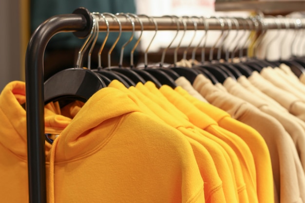 Sudaderas con capucha amarillas en perchas en un primer plano de la tienda de deportes, concepto de ropa