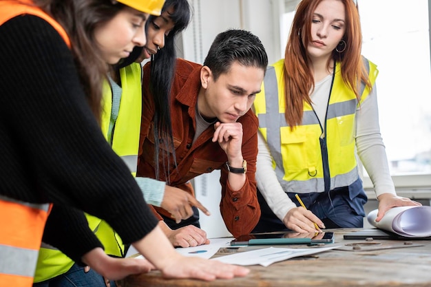 Südamerikanischer Ingenieur-Supervisor auf der Baustelle mit seinem multiethnischen Arbeitsteam, das Richtlinien im Baustellenbüro festlegt Teamwork-Konzept