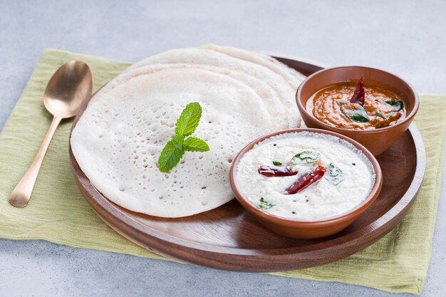 Südindisches traditionelles Frühstück Dosa oder Thattu Dosa aus Gusseisen Dosa Thawa in einem Geschirr mit Beilage, weißem Kokosnuss-Chutney und Zwiebel-Chutney auf weißem, strukturiertem Hintergrund