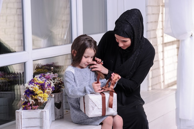 Südostasiatisches Mädchen mit Geschenkbox. Lebensstil der muslimischen Familie. Glücklich lächelnde malaiische Eltern und Kind.