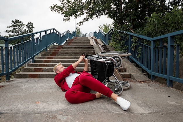 En el suelo cerca de las escaleras yace un hombre discapacitado cerca de la silla de ruedas. El concepto de silla de ruedas, persona discapacitada, vida plena, paralizada, discapacitada.