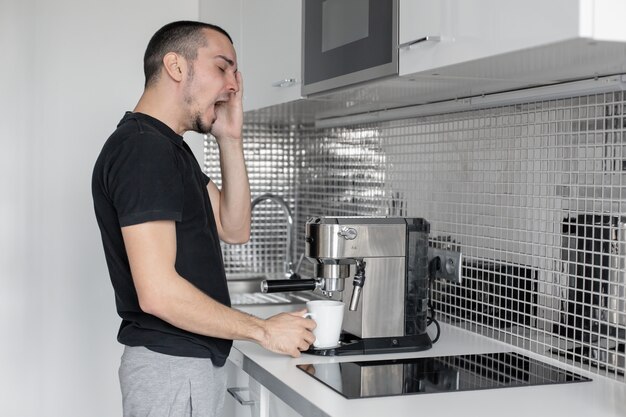 Foto sueño chico en la mañana en la cocina preparando café en una máquina de café.