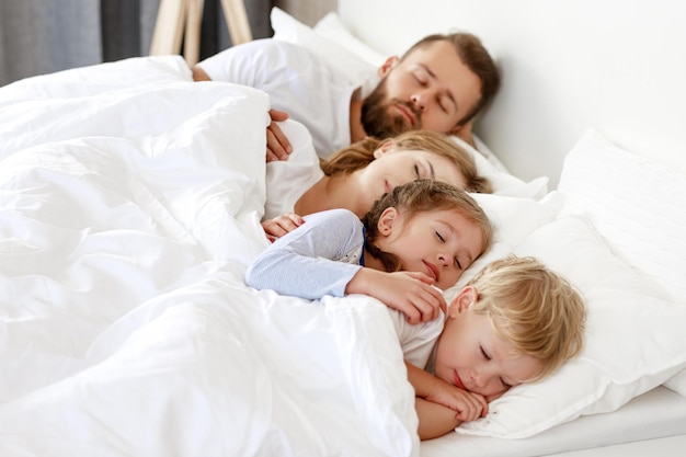 Sueño saludable padres de familia felices y niños durmiendo en una cama blanca en casa