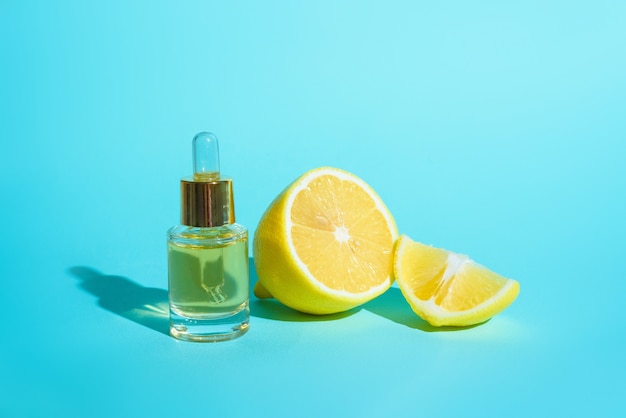 Suero facial con cítricos limón y vitamina C en frasco de vidrio con pipeta sobre fondo azul, el concepto de autocuidado de la piel en casa.