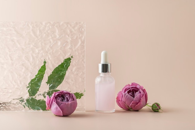 Un suero facial o aceite esencial en un frasco gotero rosa sobre un fondo beige con pétalos de rosa alrededor