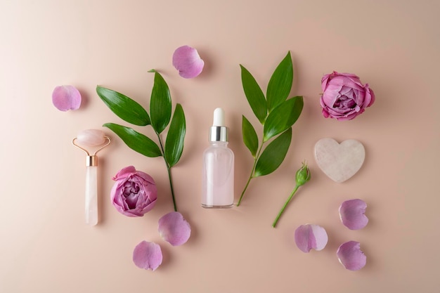Un suero facial o aceite esencial en un frasco gotero rosa sobre un fondo beige con pétalos de rosa y hojas verdes a su alrededor