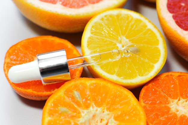 Suero facial con vitamina C con diferentes cítricos sobre un fondo blanco.