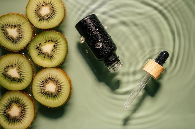 Suero de pipeta facial botella negra producto de belleza de suero de leche cerca de una rodaja de kiwi de fruta en agua salpicando una mancha transparente fresca