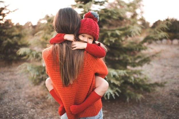 Foto süß lächelndes kind mädchen 3-4 jahre alt auf mutterhänden tragen strickmütze und pullover im freien