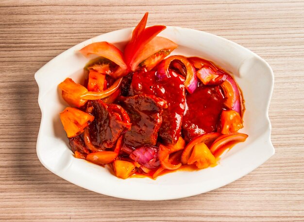 Foto süß-saure rippen mit tomaten, zwiebeln und chili-pfeffer, die in einem gericht serviert werden, isoliert auf dem tisch. blick auf das essen in hong kong