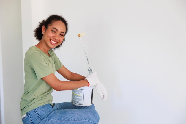 Süße afroamerikanische junge Frau hält Rollenfarbe und schmückt die Wand des neuen Zuhauses