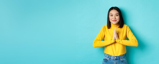 Süße asiatische Frau im trendigen Outfit, die sagt, dass Sie sich an den Händen halten, in namaste bettelnder Geste lächelnd