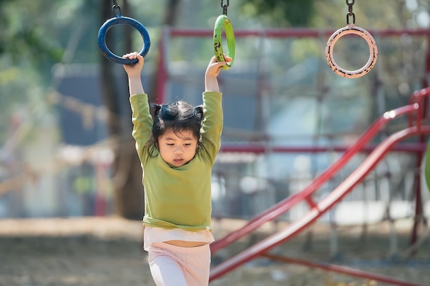 Süße asiatische Mädchen Lächeln spielen Klettern Sie die Bar auf Schule oder Kindergarten Hof oder Spielplatz Gesunde Aktivität Kinder Kleines Mädchen Klettern im Freien auf dem Spielplatz Kind spielt auf Spielplatz im Freien