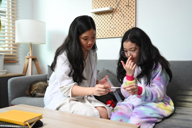 Süße asiatische Mädchen medizinische Uniform spielt als Ärztin mit ihrer jungen Schwester zu Hause