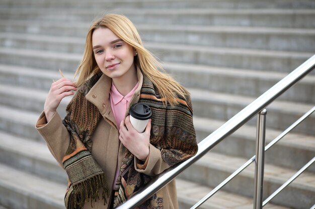 Süße Blondine in der Stadt trinkt Kaffee auf der Treppe