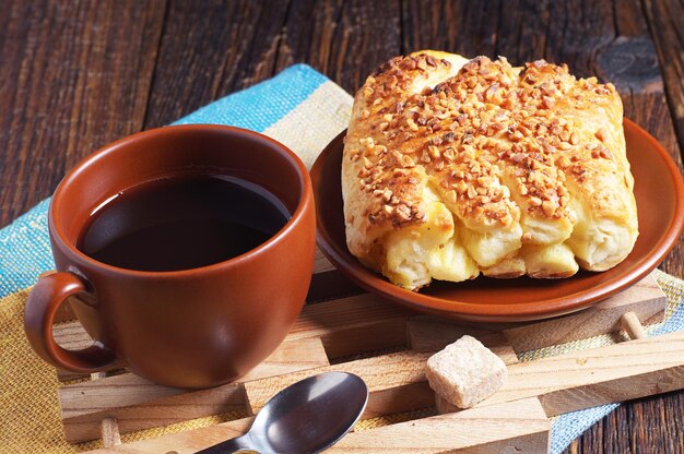 Süße Brötchen mit Nüssen und schwarzem Kaffee zum Frühstück auf einem dunklen Holztisch