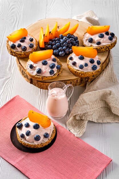 Süße Brötchen mit Weichkäse, Blaubeere und Scheibe der Persimone auf weißem Holztisch