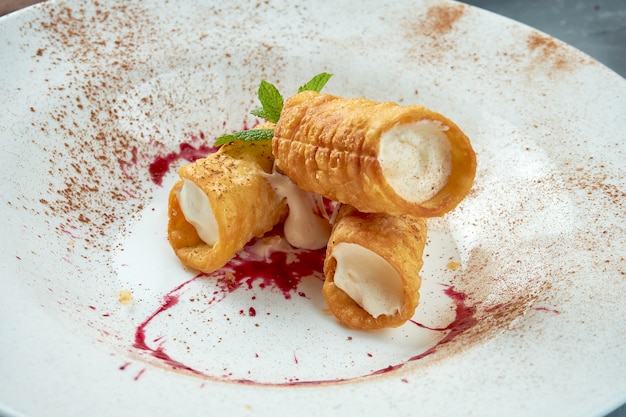 Süße Cannoli gefüllt mit Ricotta, Beerensauce und Kakao in einem weißen Teller. Italienisches Dessert