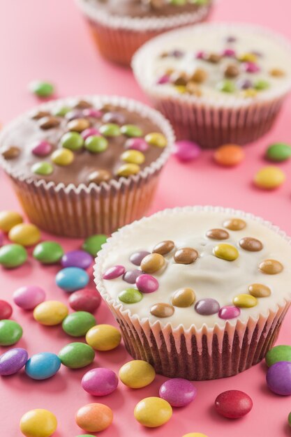 Süße Cupcakes mit Süßigkeiten auf rosa Hintergrund