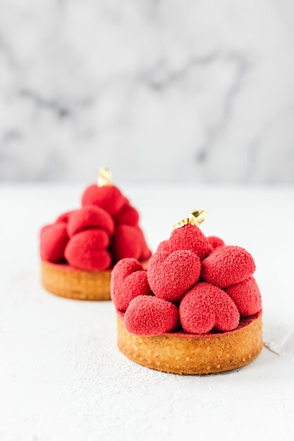 Süße Desserttartelettes mit roten Mousseherzen an der Spitze