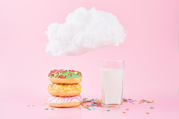 Süße Donuts mit Sprinkel und Milch unter einer kleinen Wolke auf einem rosa Hintergrund. Verschiedene dekorierte Donuts als Konzept für ein frisches leckeres Frühstück.