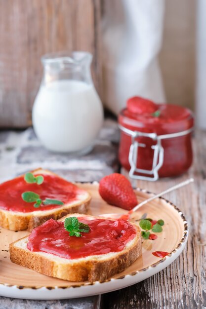 Süße Erdbeermarmelade auf Toastnahaufnahme. Selektiver Fokus. Der Snack ist mit Minzblättern, vertikalem Rahmen und Nahaufnahme dekoriert. Idee für Frühstück oder Mittagessen